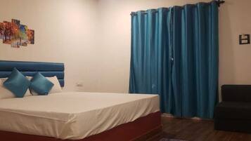 Un dormitorio con cama, ventilador de techo, cortina azul y una alfombra pequeña.