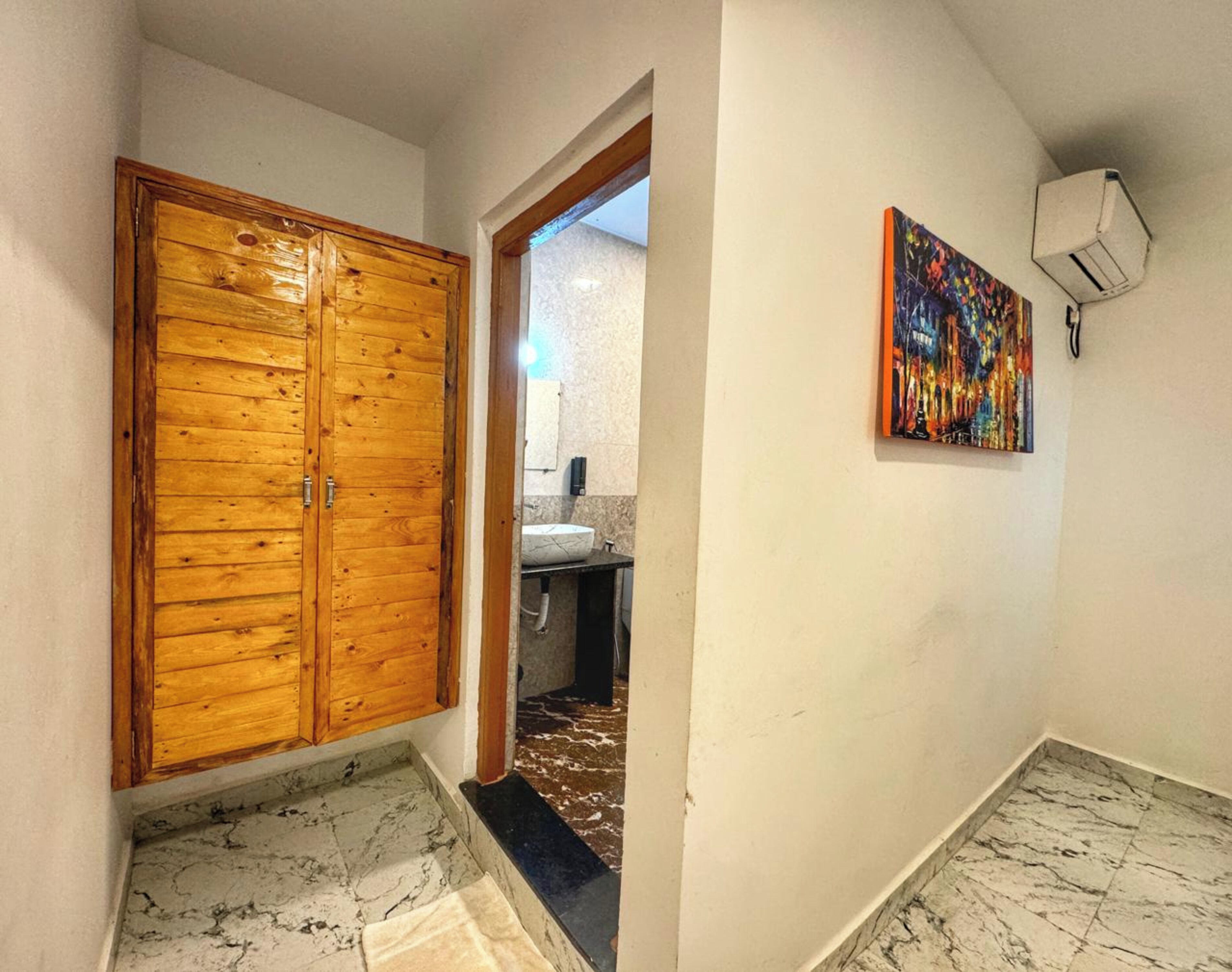 A hallway with a wooden door, a bathroom with a sink and mirror, and a colorful painting on the wall.