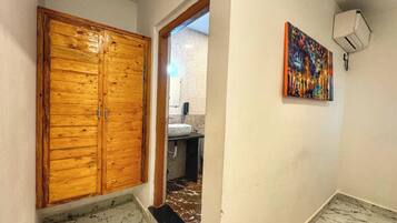 A hallway with a wooden door, a bathroom with a sink and mirror, and a colorful painting on the wall.