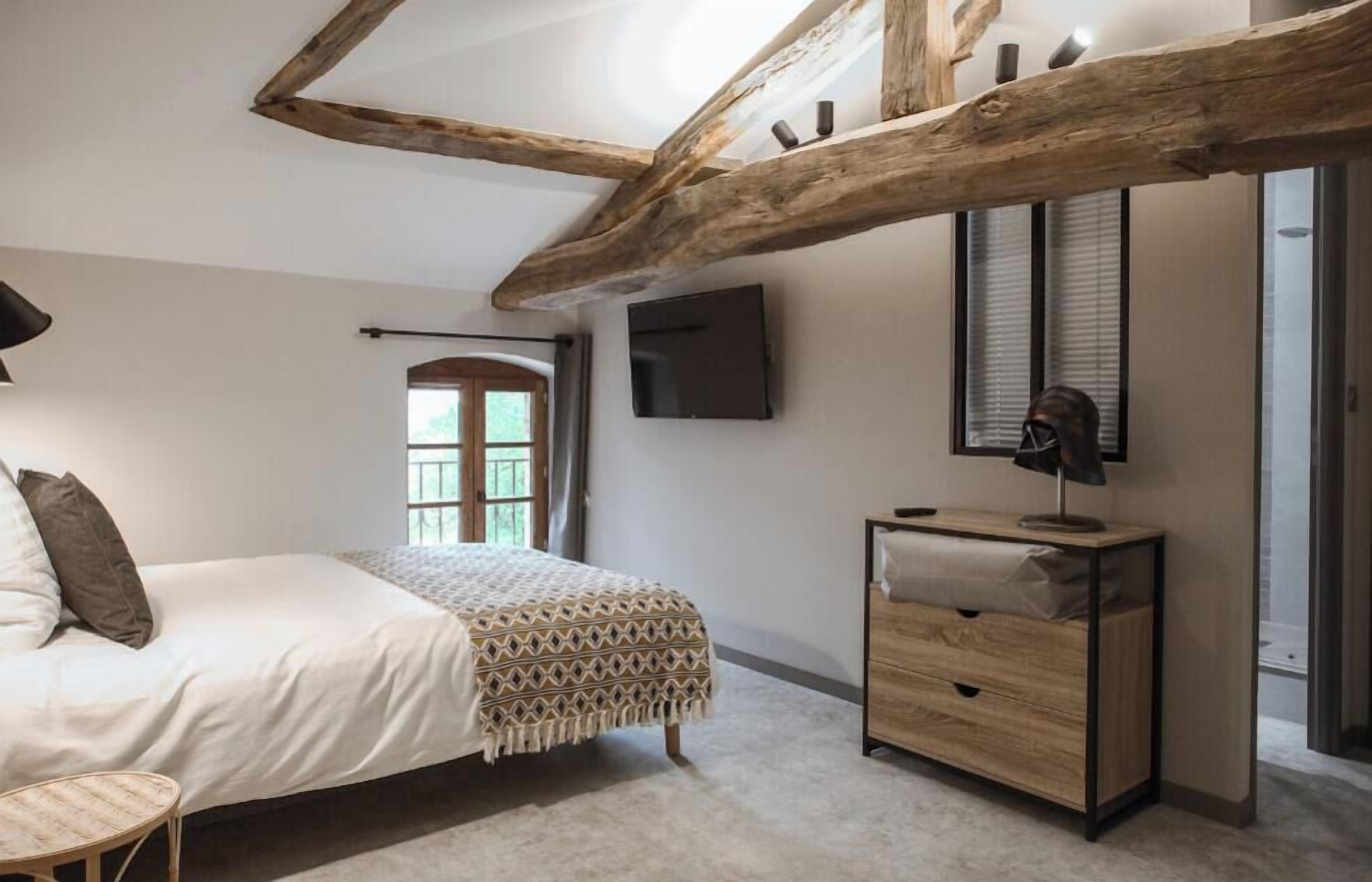 Ein Schlafzimmer mit einem Bett, einem Nachttisch, einer Lampe, einem Fernseher und einem Fenster mit Jalousien.