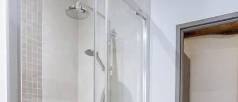 Un espace douche fermé par des parois de verre, avec un mur carrelé, une pomme de douche et un panneau de commande.