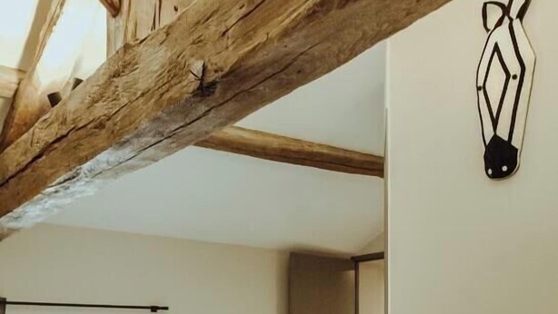 Una stanza con un divano marrone, una trave in legno a soffitto, una finestra e un lampadario a parete.