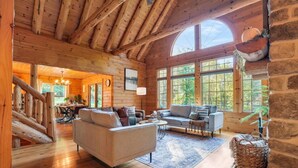 Ein Holzblockhaus-Interieur mit Holzbalkendecke, großen Fenstern, einer Couch und einem Essbereich.