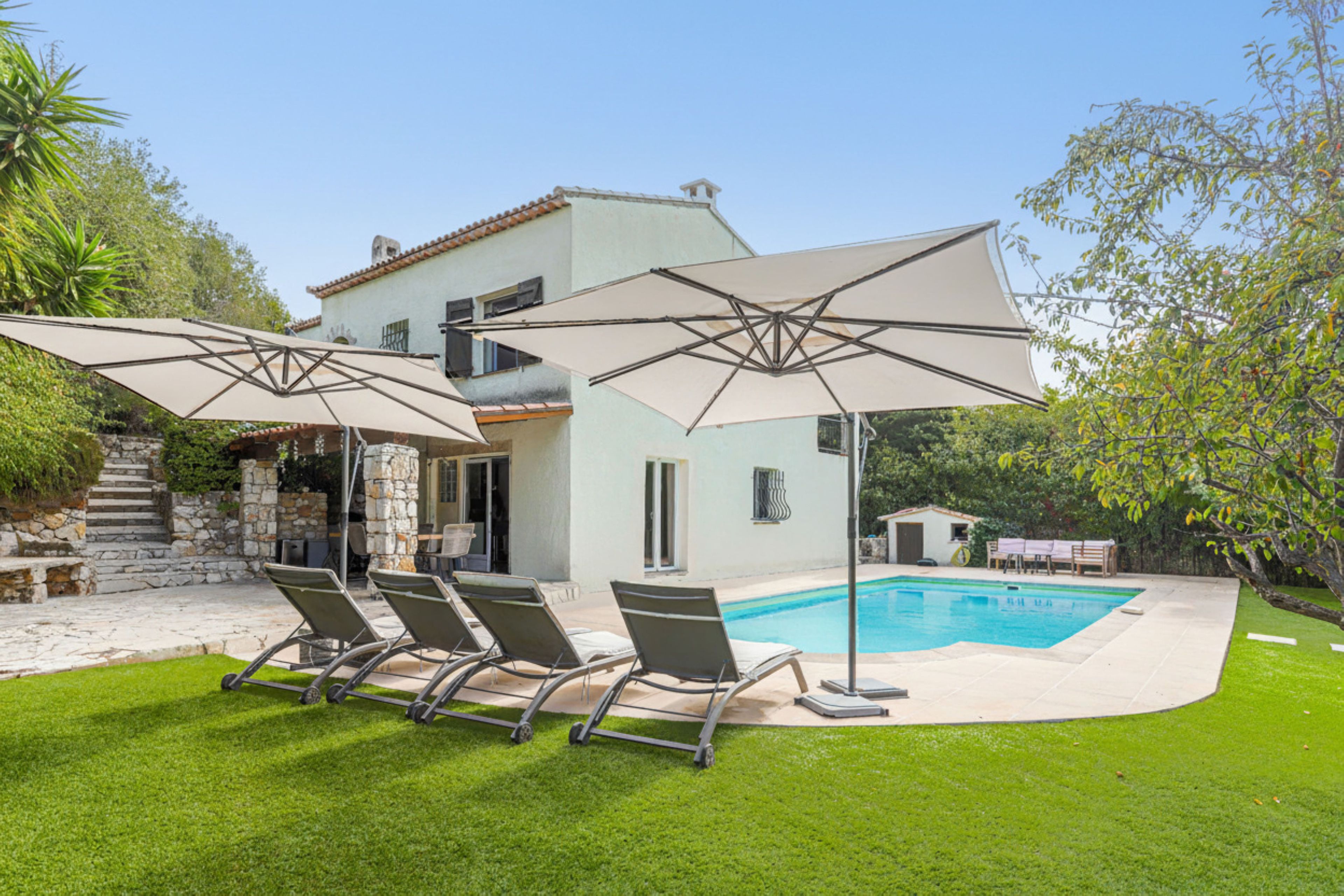 A two-story house with a swimming pool, outdoor seating, and a stone staircase.