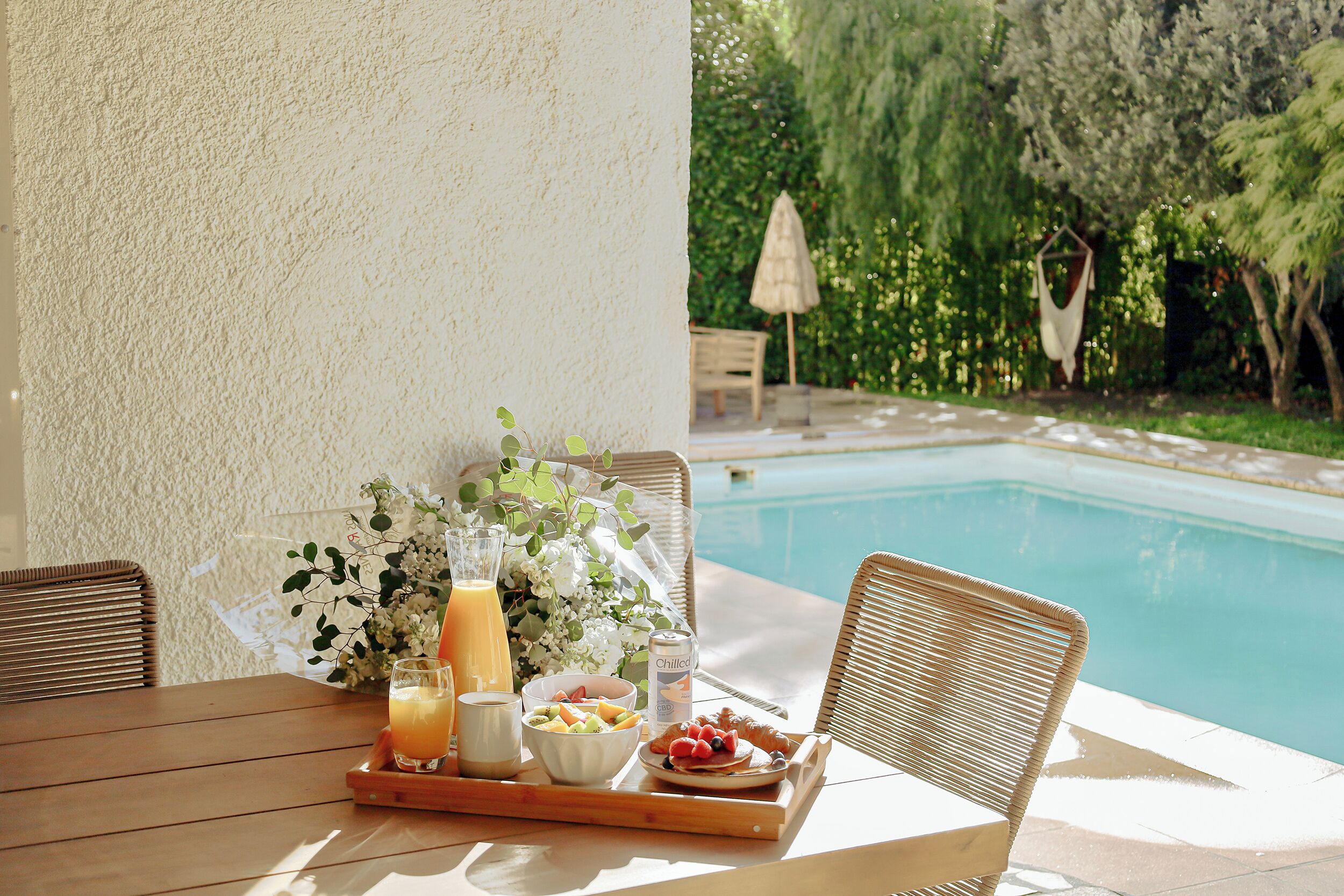 A wooden table with a tray containing a glass of orange juice, a bowl of fruit, a glass of milk, and a can of Chilled coffee.