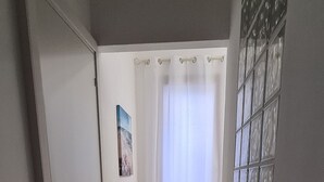 Ein Flur mit einer Tür links, einem Fenster mit Vorhängen rechts und einer Wand mit einer Zierleiste.