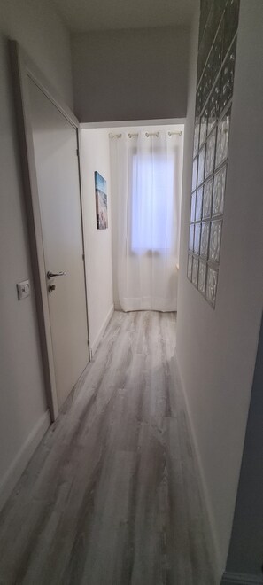 A hallway with a door on the left, a window with curtains on the right, and a wall with a decorative panel. - Double Paradise in the center (Cagliari)