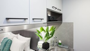 A modern kitchen with white cabinets, a stainless steel range hood, a sink, and a potted plant.