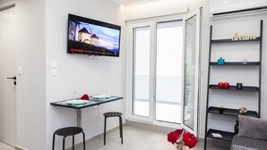 A modern room with a dining table, two chairs, a TV mounted on the wall, a small round table with a vase of red roses, and a bookshelf with decorative items.