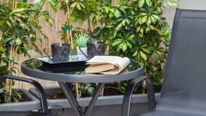 A round metal table with a tray, two black mugs, a white mug, a small potted plant, and an open book.
