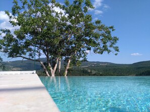 A clear swimming pool with a tree in the background and a view of hills. - Agriturismo Tenuta il Polardo - Appartamento Piano Terra (Piegaro)