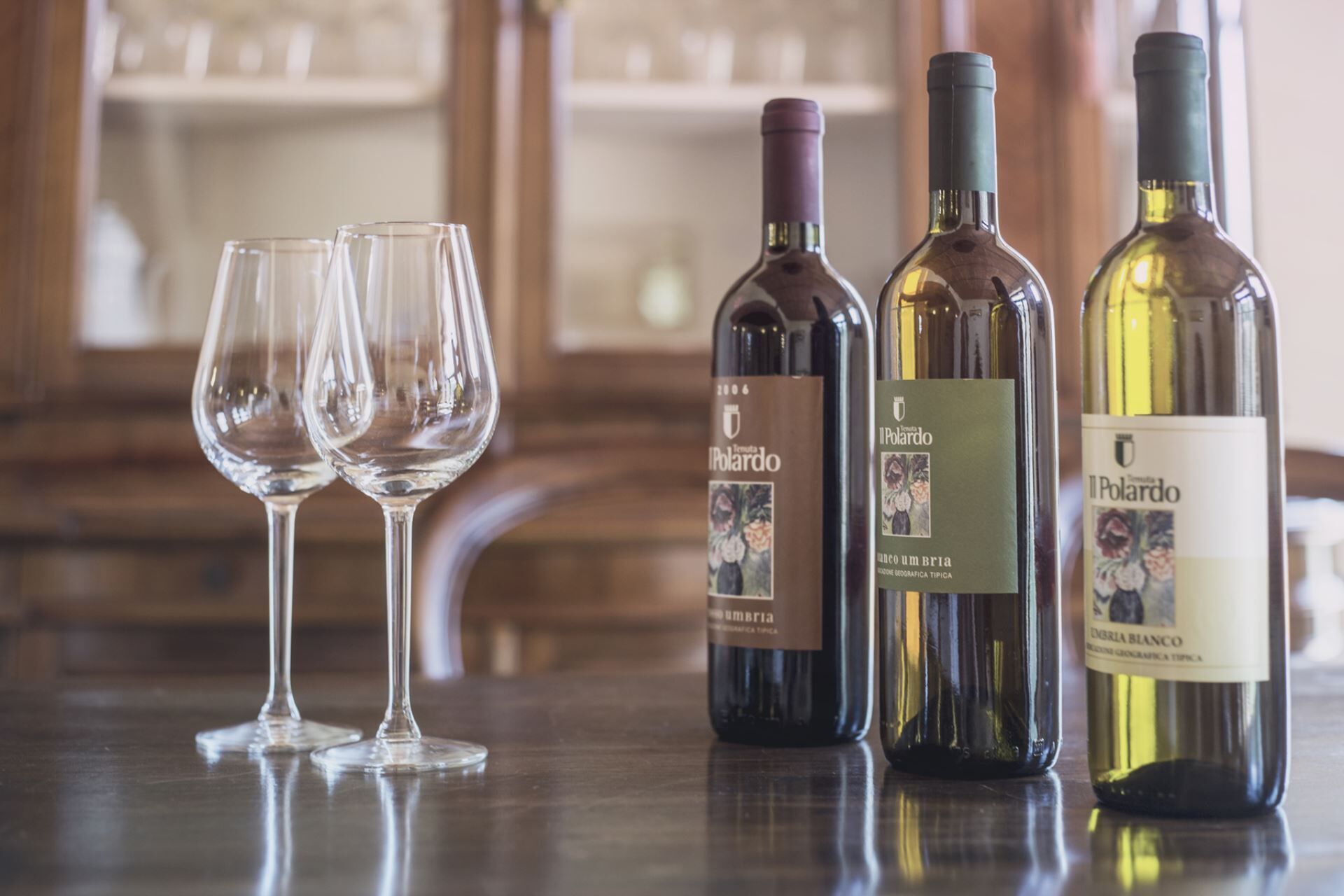 Three wine bottles and two empty wine glasses on a wooden table.