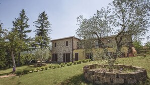 Un bâtiment en pierre à la façade jaune, entouré d’un jardin bien entretenu et d’arbres.