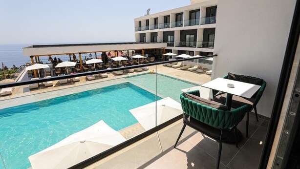 A poolside area with a view of the sea, a lounge with chairs and umbrellas, and a building with balconies. - Black Diamond Hotel Dhermi (Himarë)
