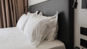 A neatly made bed with white linens and pillows, a dark headboard, and a wall-mounted light fixture. - Black Diamond Hotel Dhermi (Himarë)