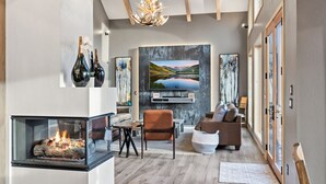 Ein modernes Wohnzimmer mit Kamin, bequemen Sitzgelegenheiten, Kunstwerken an den Wänden und einem großen Fenster für natürliches Licht.