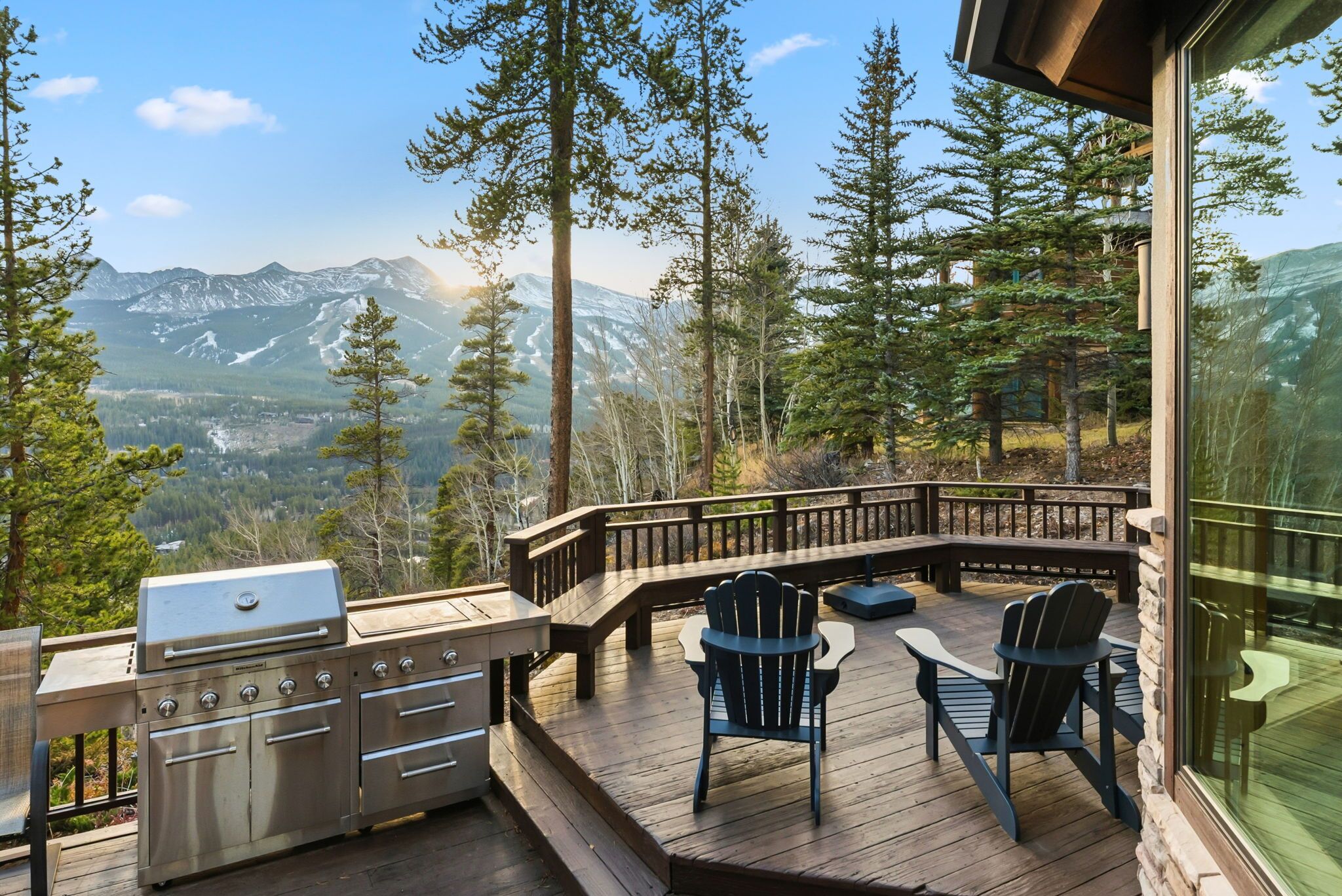 A deck with a grill and chairs, overlooking a mountainous landscape.