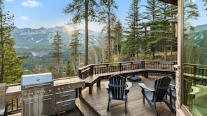 Eine Terrasse mit Grill und Stühlen mit Blick auf eine gebirgige Landschaft.