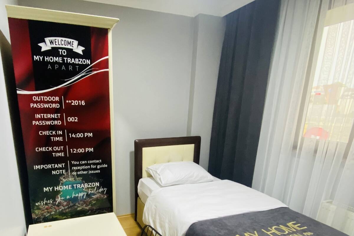 Quarto de hotel com uma cama, uma escrivaninha, um controle remoto e uma placa de boas-vindas.