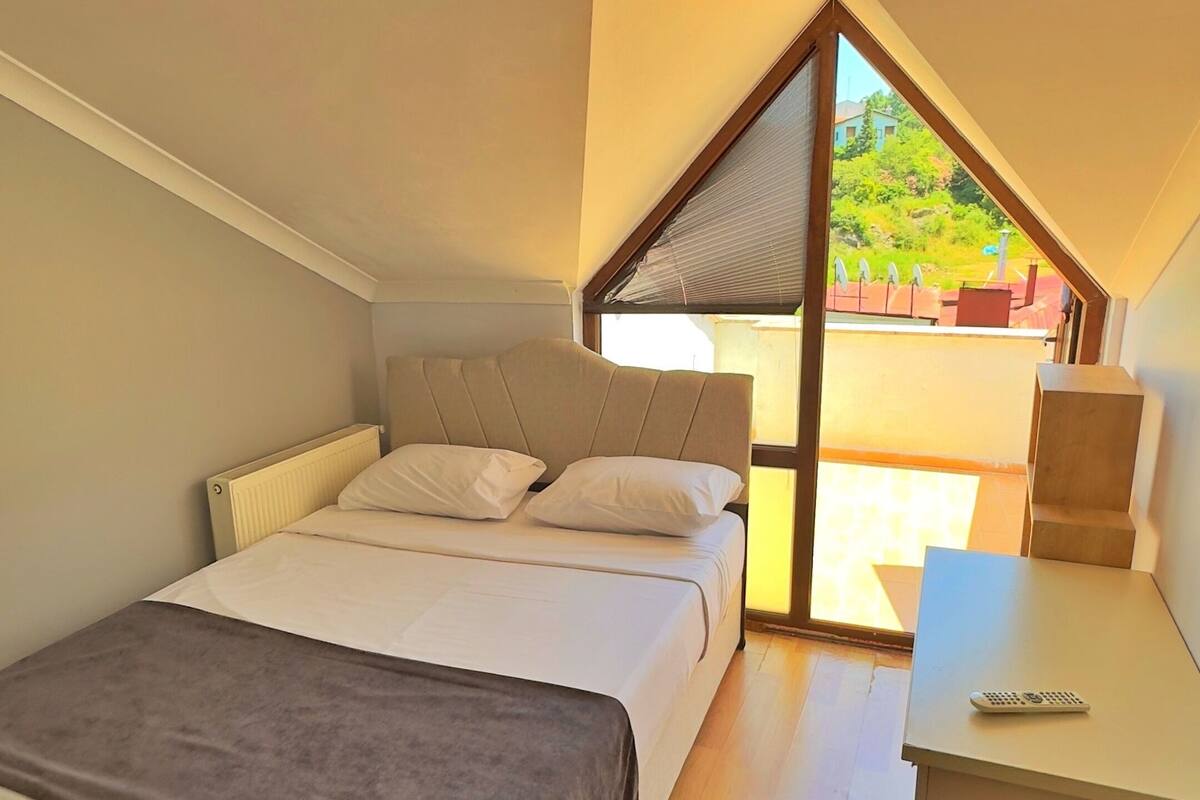 Quarto com cama, escrivaninha e vista para o exterior.