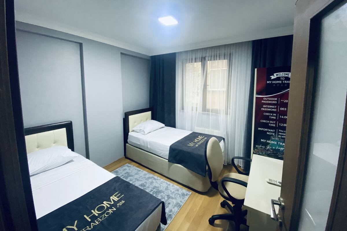 Quarto de hotel com duas camas, uma escrivaninha, uma cadeira e uma janela com cortinas.