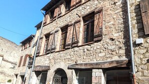 A stone building with wooden shutters, a metal gate, and a shop with various items displayed outside. - Apartment Le Saint Jean 2 Confort et Cosy Résidence Les Rosalys (Villefranche de Conflent)