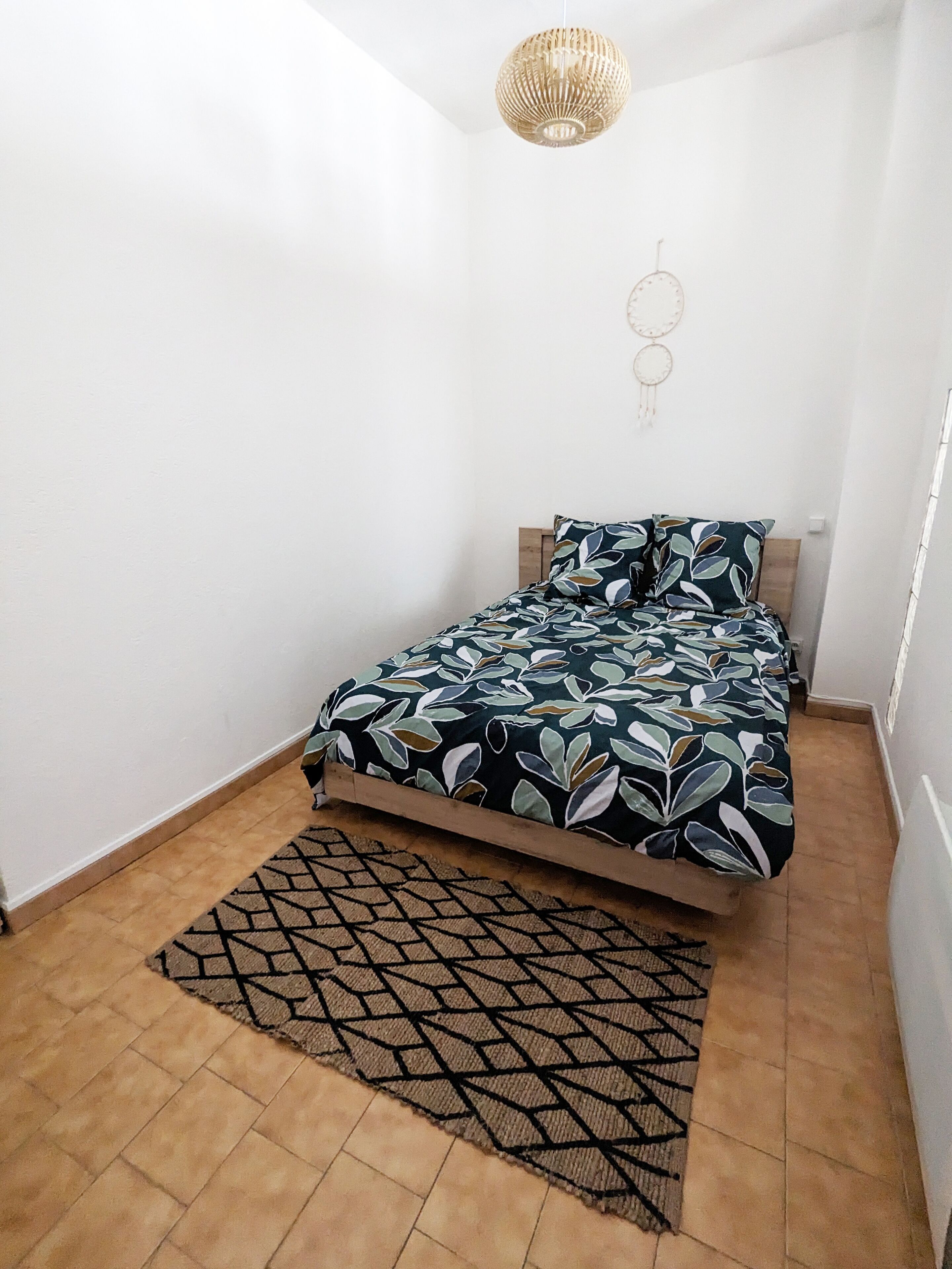 Ein Schlafzimmer mit Bett, einem gemusterten Teppich und einer Hängelampe.