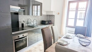 A modern kitchen with stainless steel appliances, a dining area with a table set for two, and a large window with curtains. - Apartment Le Saint Jean 2 Confort et Cosy Résidence Les Rosalys (Villefranche de Conflent)