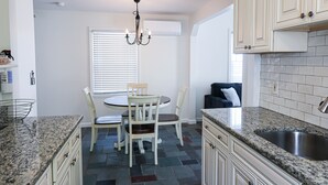 A kitchen with a granite countertop, a dining table with chairs, a chandelier, and a built-in sink.