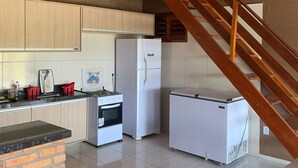 Een compacte keuken met houten kastjes, een koelkast, een fornuis en een kleine koelkast. Een houten trap leidt naar een hoger gelegen verdieping.