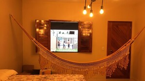 Een kamer met een hangmat, een bed met bloemenbeddengoed en een televisie waarop een uitzicht te zien is.
