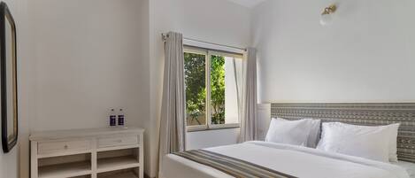 A bedroom with a bed, a nightstand, a window with curtains, and a wall-mounted light fixture.