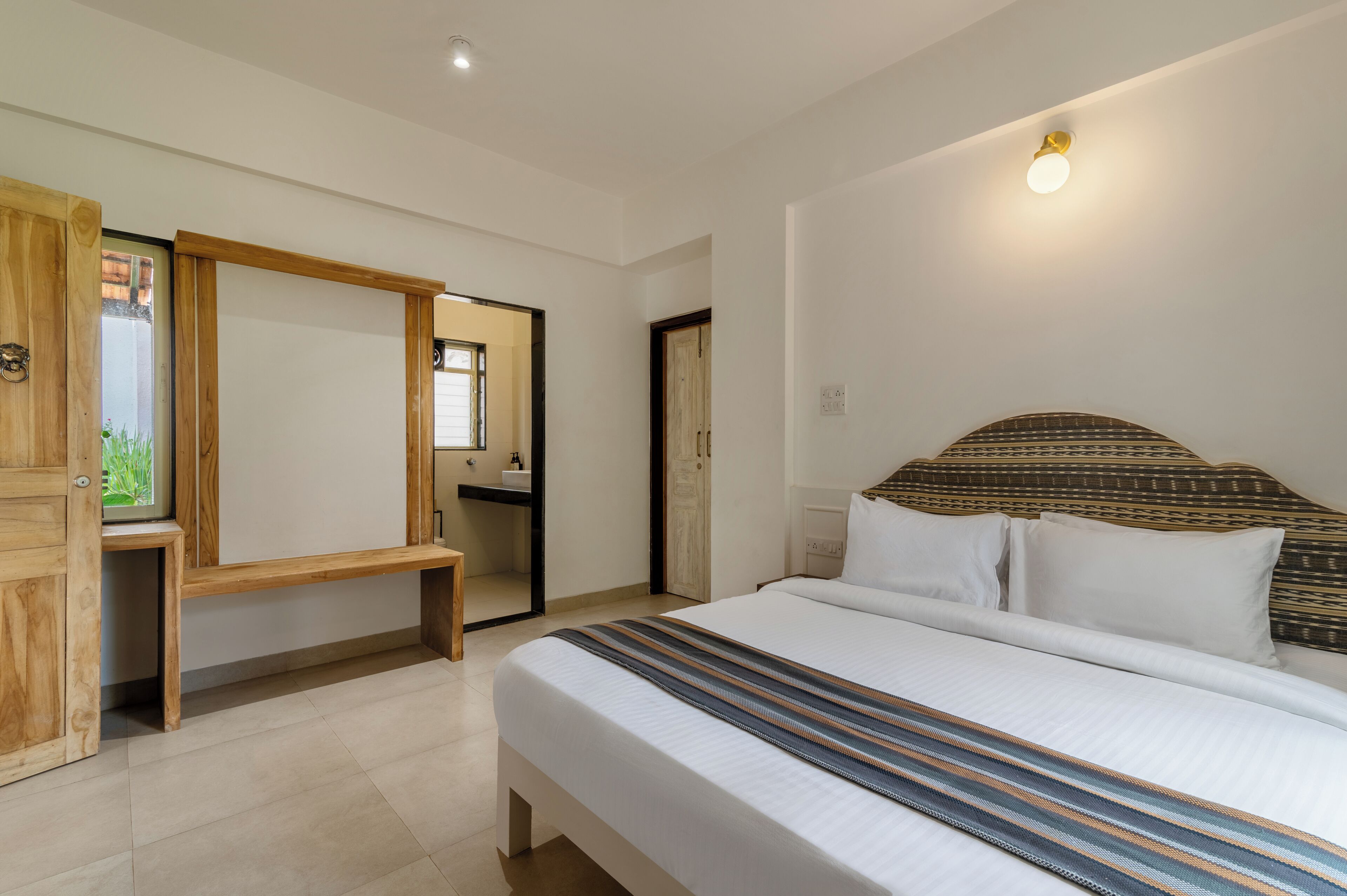 A bedroom with a large bed, a wooden wardrobe, a mirror, and a small bench.