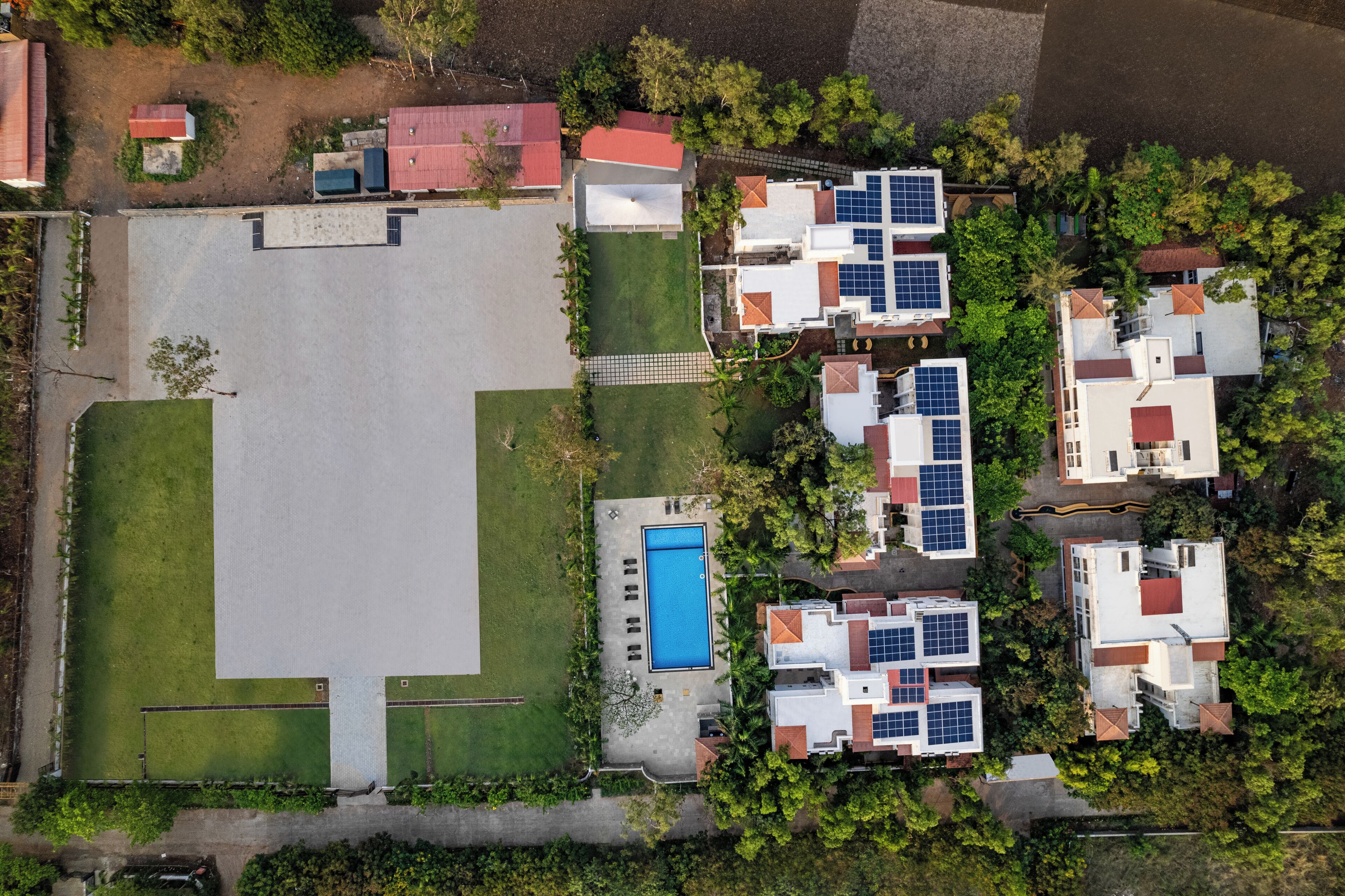 An aerial view of a residential area with houses, solar panels, a swimming pool, and green spaces.