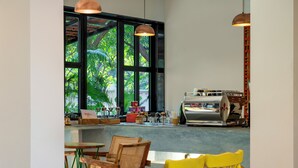Un café avec des meubles en bois, une machine à café et de grandes fenêtres donnant sur un paysage verdoyant.