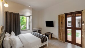 Une chambre d’hôtel équipée d’un lit, d’un bureau, d’une télévision et d’une porte en bois donnant sur un espace extérieur.
