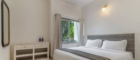 A bedroom with a bed, a bedside table, a window with curtains, and a wall-mounted light fixture.