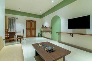 Ein modernes Wohnzimmer mit Couchtisch aus Holz, zwei Sessel, einem Fernseher und einem Essbereich mit Tisch und Stühlen.