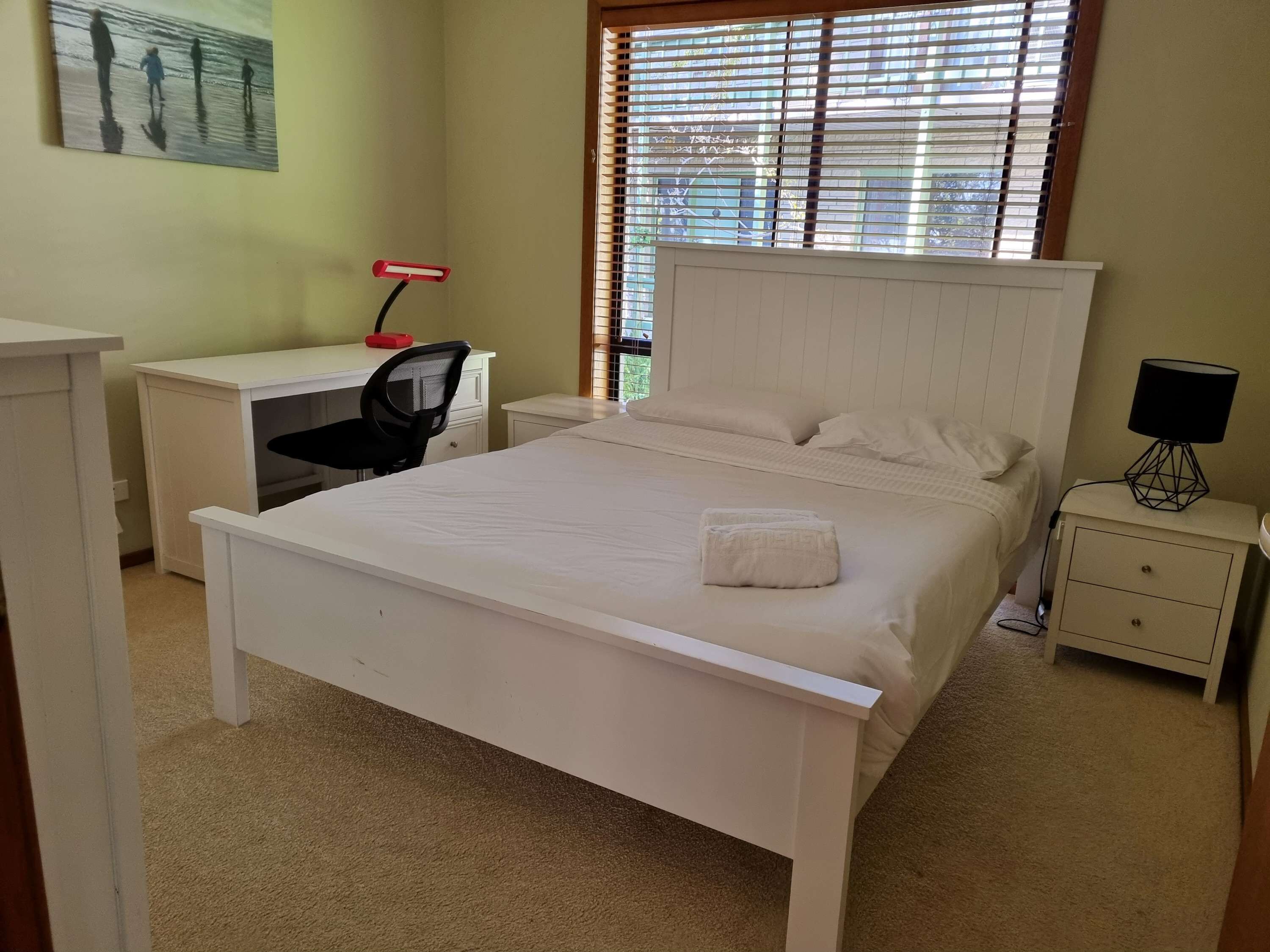Een slaapkamer met een bed, een bureau, een stoel, een nachtkastje en een lamp.
