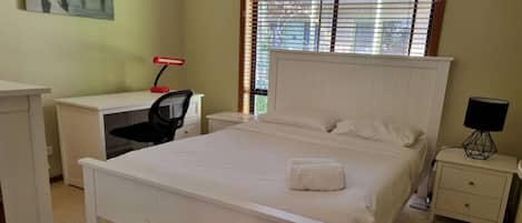 Een slaapkamer met een bed, een bureau, een stoel, een nachtkastje en een lamp.