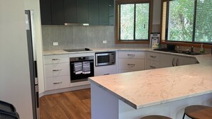 Een moderne keuken met donkere kastjes, een groot eiland met barstoelen en uitzicht op groen.