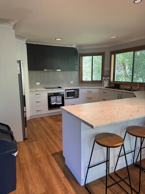 A modern kitchen with dark cabinets, a large island with bar stools, and a view of greenery outside.