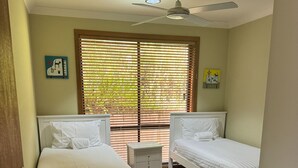 Een slaapkamer met twee bedden, een plafondventilator en een raam met zonwering.