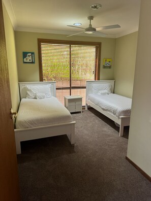 A bedroom with two beds, a ceiling fan, and a window with blinds.