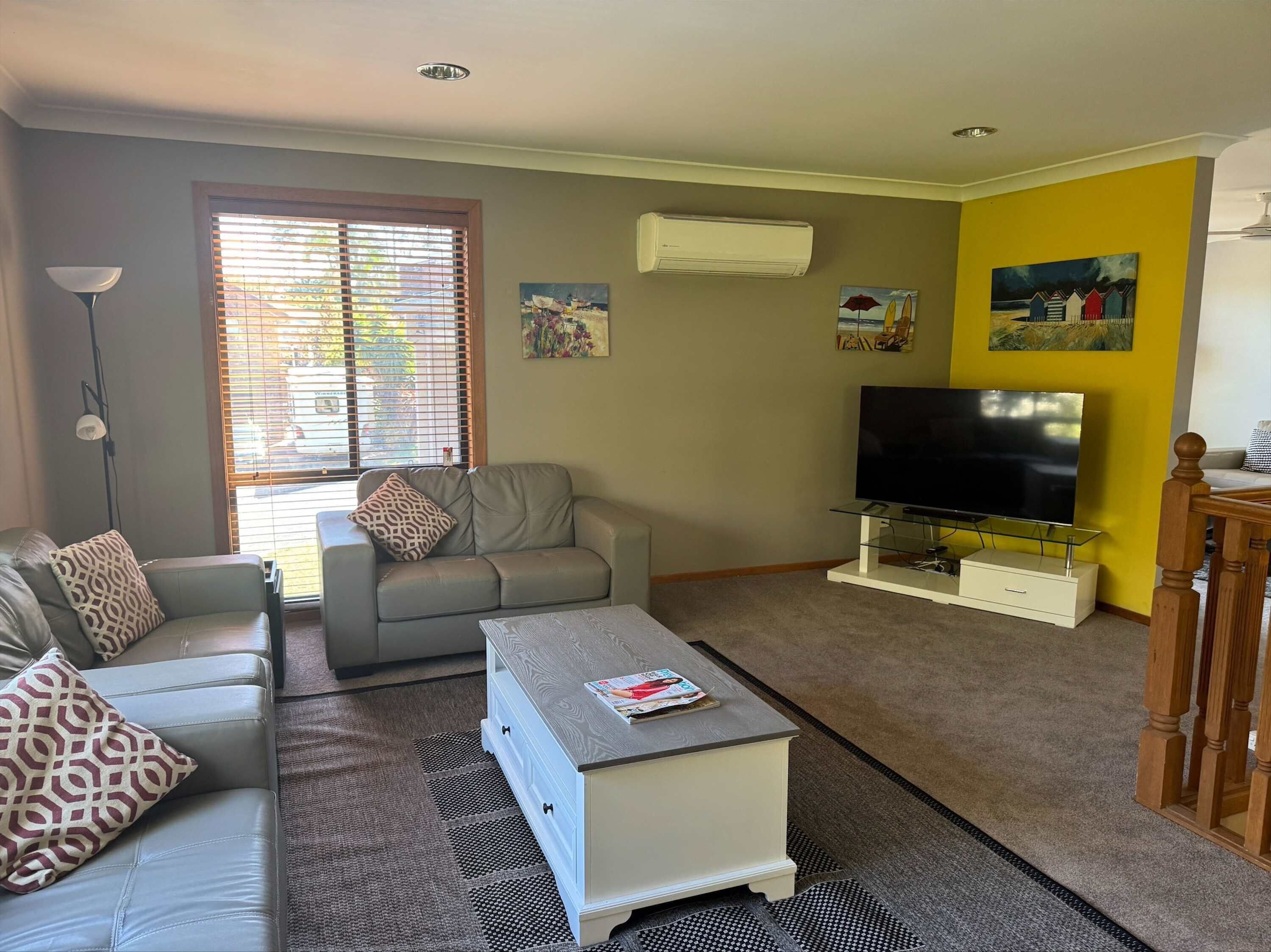 A living room with a sofa, a coffee table, a TV on a stand, and artwork on the walls.