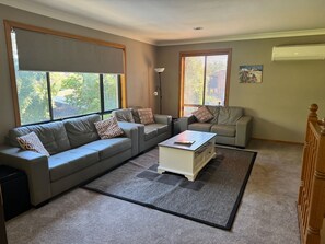 A living room with a grey sofa, a smaller grey sofa, a coffee table, and a rug. - 5BR Family Retreat Steps to Beach - High Tide (Lilli Pilli)