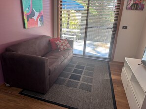 Una sala de estar con un sofá marrón, un tapete estampado, un mueble blanco y un ventanal con persianas.