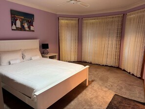 Une chambre à coucher avec un grand lit, une table de chevet avec une lampe et deux fenêtres ornées de rideaux légers.
