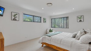A bedroom with a bed, two windows with blinds, and three framed pictures on the wall. - Relax at the Park by Book Jervis Bay (Sanctuary Point)