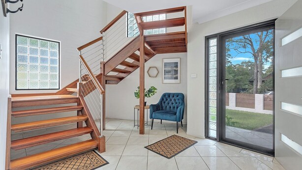A modern interior with a wooden staircase, a blue armchair, and a view through a glass door. - Relax at the Park by Book Jervis Bay (Sanctuary Point)